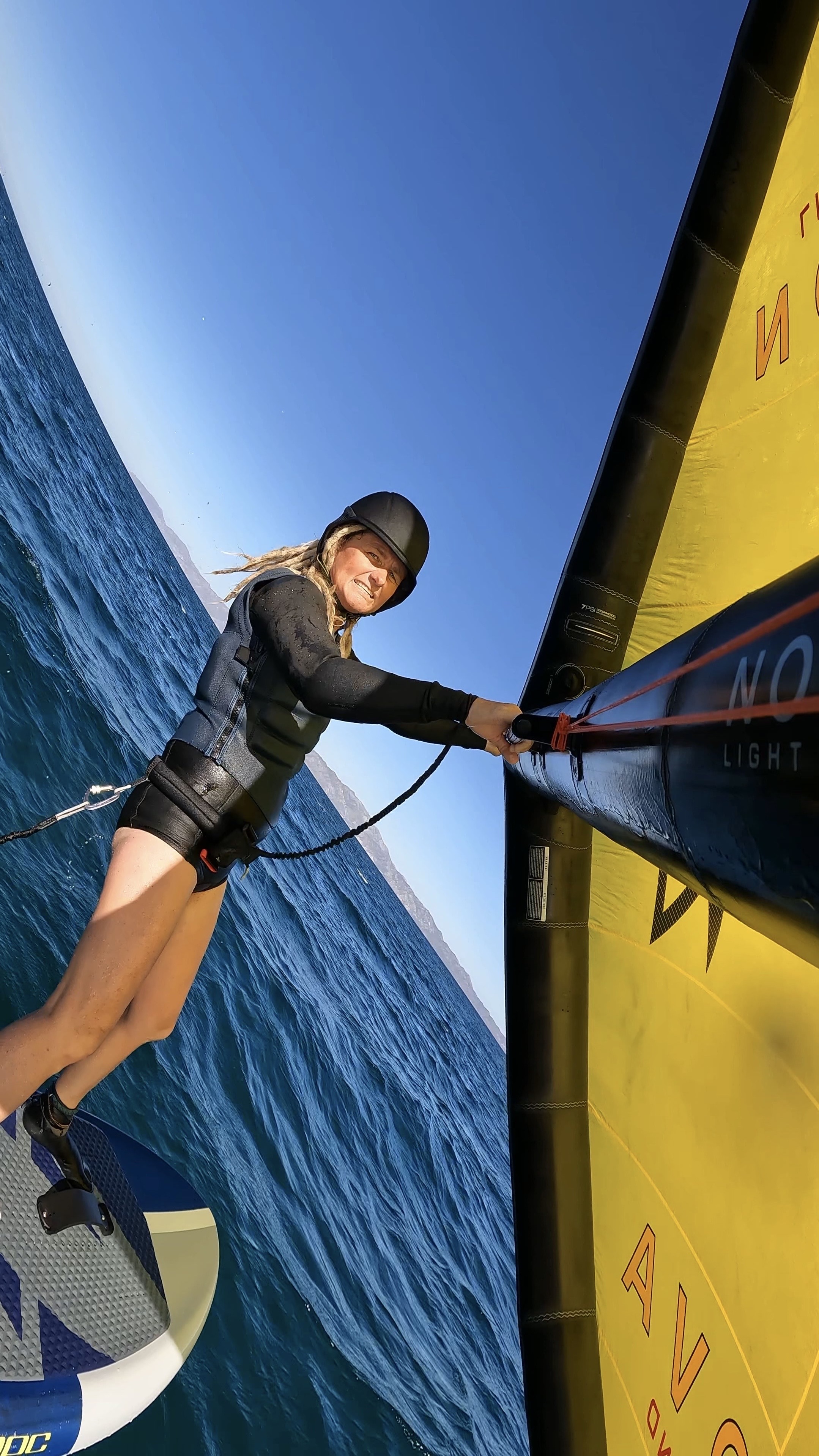 Woman wing-foiling with yellow wing in tropical waters wearing a shorty wetsuit